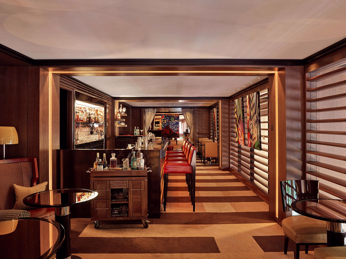 Symmetrische Innenansicht der BAR45 im 45 Park Lane mit Blick entlang der hölzernen Lamellenfenster, den roten Lederhockern an der Bar und gemütlichen runden Bistrotischen in warmem, gedimmtem Licht