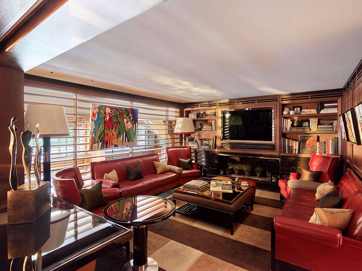 Der einladende Bibliotheksbereich der BAR45 im Hotel 45 Park Lane mit tiefroten Ledersofas, einem dunklen Couchtisch voller Bildbände, eingebauten Bücherregalen und einem großen Fernsehbildschirm