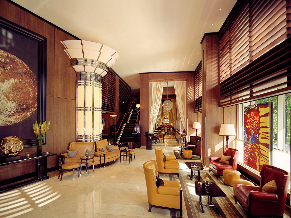 Weitwinkelansicht der luxuriösen Lobby-Lounge im 45 Park Lane mit hohen Decken, edler Holzvertäfelung, einer Mischung aus gelben und roten Ledersesseln sowie einem Blick auf den tiefen Restaurantbereich im Hintergrund