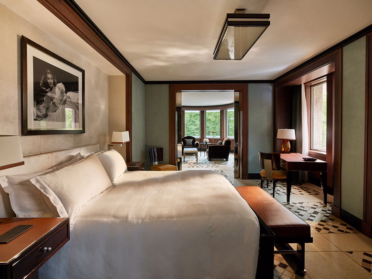 Ein elegantes Executive King Zimmer im Hotel 45 Park Lane mit einem großen Doppelbett, einer ledernen Sitzbank am Fußende, einem klassischen Schwarz-Weiß-Porträt an der Wand und einem hölzernen Schreibtisch am Fenster