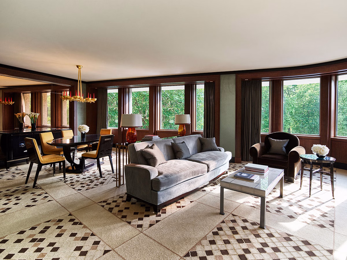 Das großzügige Wohnzimmer der Park Suite im 45 Park Lane mit einem gemusterten Teppichboden, einem samtgrauen Sofa, einem angrenzenden Essbereich mit dunklem Holztisch und einer Fensterfront zum Hyde Park