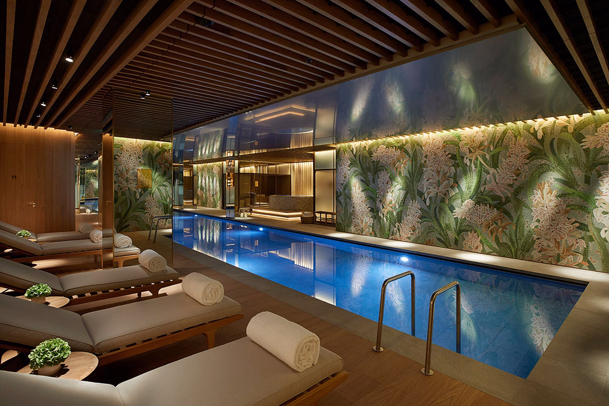 Der stimmungsvoll beleuchtete Indoor-Pool im Spa des Hotels 45 Park Lane mit komfortablen Holzliegen, einer Deckenverkleidung aus dunklen Holzlamellen und einer kunstvollen Mosaikwand mit floralen Motiven