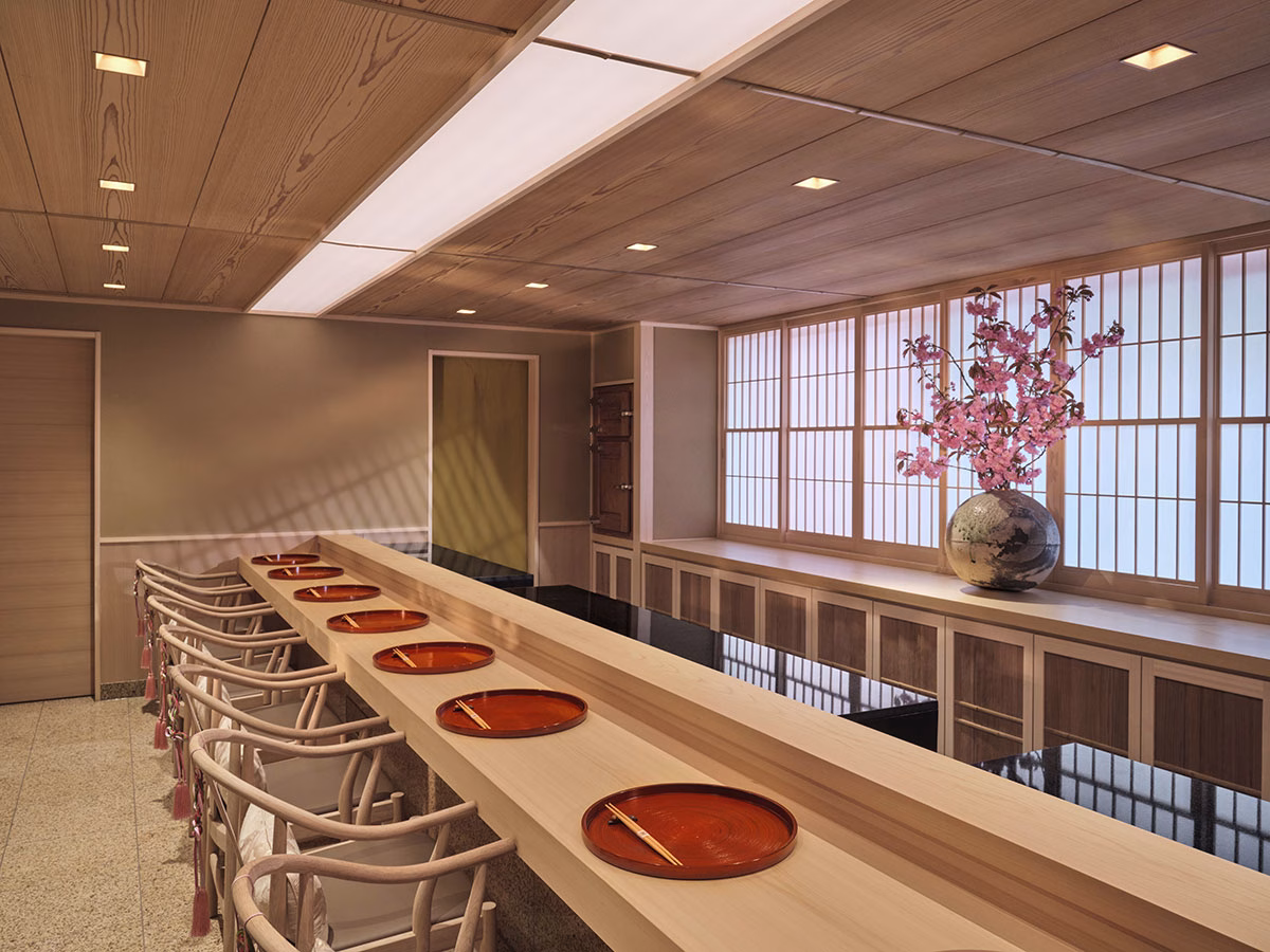 Das exklusive Restaurant Sushi Kanesaka im 45 Park Lane im minimalistischen japanischen Design mit einer langen Massivholztheke, runden roten Lacktellern und einer Vase mit blühenden Kirschzweigen vor Shoji-Schiebewänden