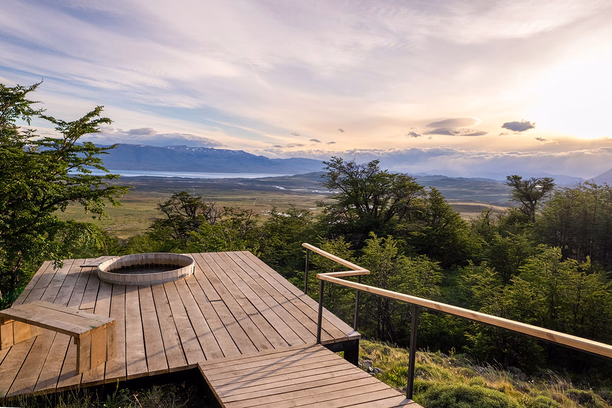 Ein runder Holz-Whirlpool auf einer freistehenden Aussichtsplattform aus Holzbohlen im Awasi Patagonia mit weitem Blick über Bäume und Steppenlandschaft im Abendlicht