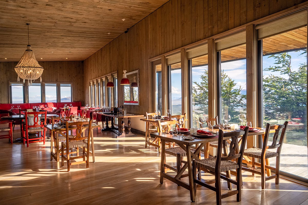 Lichtdurchfluteter Speisesaal des Restaurants im Awasi Patagonia mit Holzwänden und -böden, elegant eingedeckten Tischen und einer großen Panoramafensterfront mit Blick auf Bäume und die patagonische Landschaft