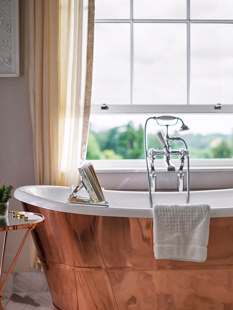 Detailaufnahme einer freistehenden, glänzenden Kupfer-Badewanne in der Arbuthnot Suite im Coworth Park, direkt platziert vor einem großen Fenster mit Ausblick auf die Parklandschaft