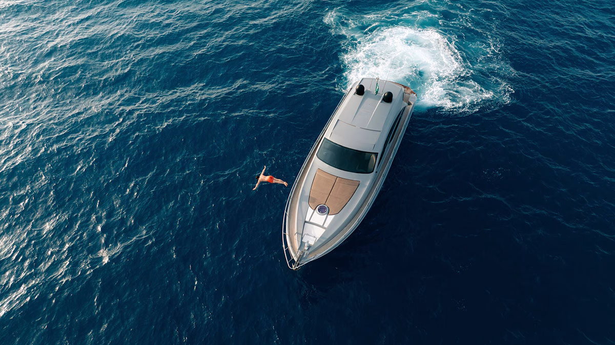Luftaufnahme einer modernen, silberfarbenen Luxusyacht auf dem tiefblauen Meer nahe dem Four Seasons AMAALA, während eine Person im Wasser daneben schwimmt