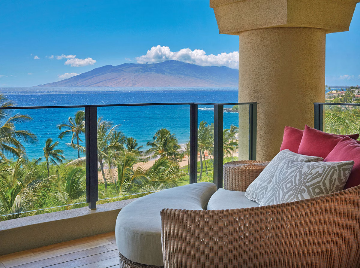 Luxuriöses Daybed aus Korbgeflecht auf einem privaten Balkon im Four Seasons Maui at Wailea mit spektakulärem Blick über Palmen hinweg auf das blaue Meer und eine Nachbarinsel