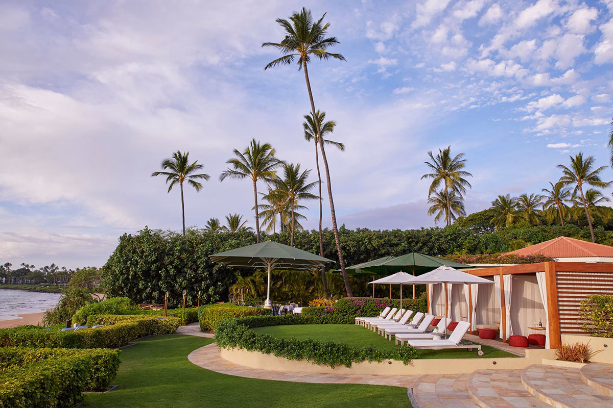 Rasenfläche im Außenbereich des Four Seasons Maui at Wailea mit weißen Sonnenliegen, Sonnenschirmen und privaten Cabanas unter hohen Palmen