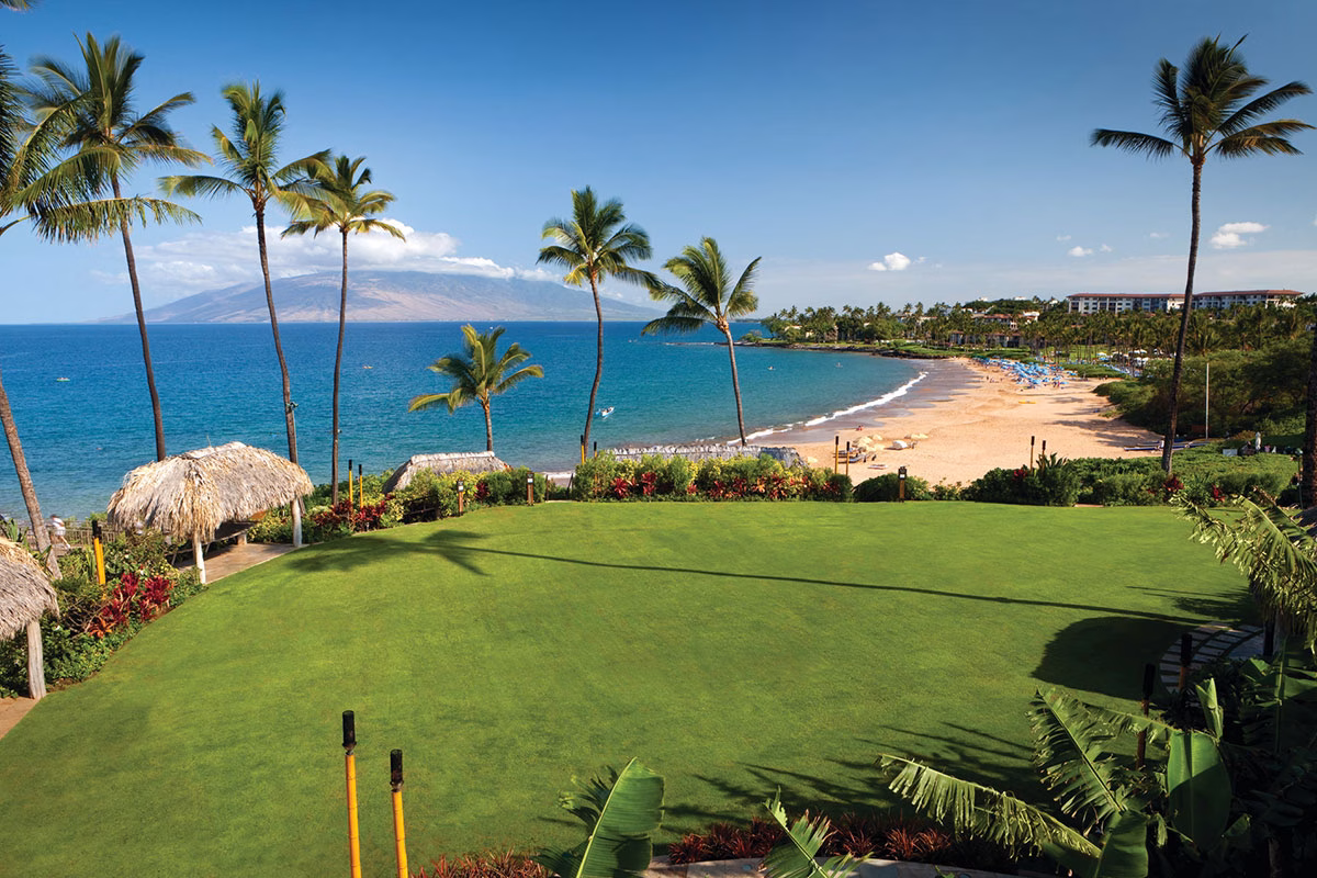 Eine perfekt gepflegte, grüne Rasenfläche im Four Seasons Maui at Wailea, die an den Sandstrand und das türkisfarbene Meer grenzt