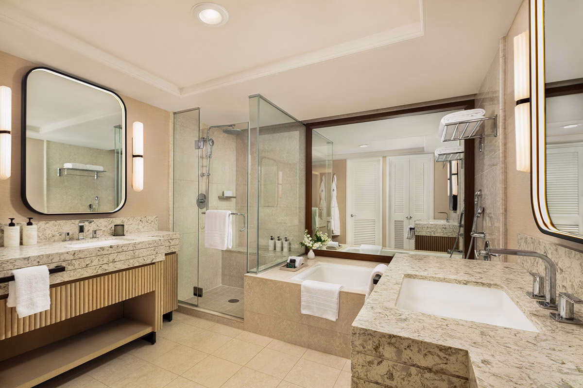 Modernes, elegantes Badezimmer im Hotel Four Seasons Oahu mit hellem Marmor-Doppelwaschtisch, einer separaten Badewanne und einer gläsernen Walk-in-Dusche mit stilvoller Beleuchtung