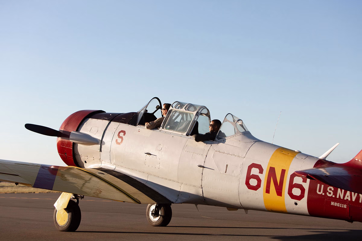 Zwei Männer sitzen im Cockpit eines historischen Propellerflugzeugs der US Navy auf dem Rollfeld, aufgenommen während eines Ausflugsprogramms des Four Seasons Oahu
