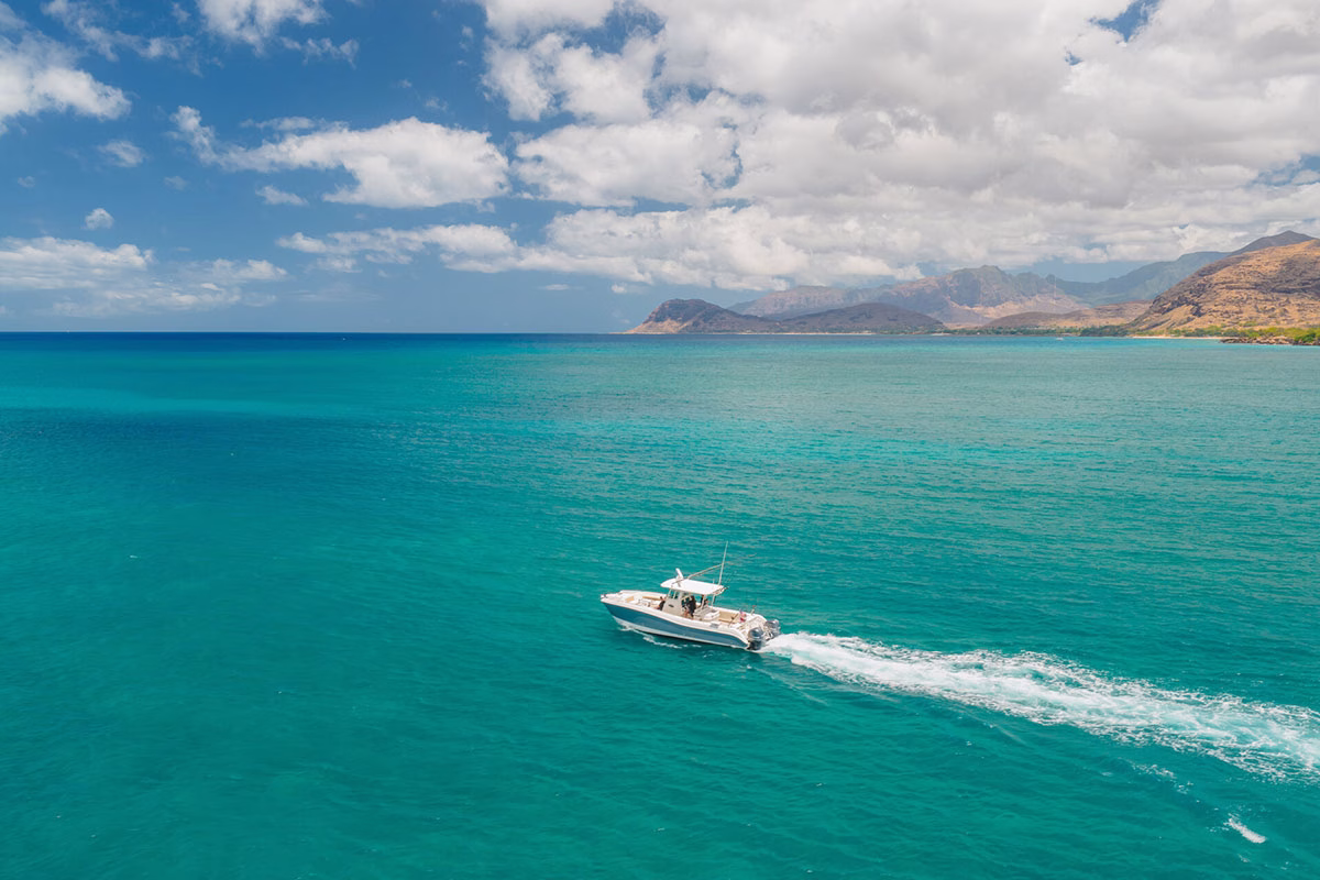 Ein weißes Motorboot fährt bei einem vom Four Seasons Oahu organisierten Ausflug durch das kristallklare, türkisblaue Wasser vor der malerischen Bergkulisse der Insel