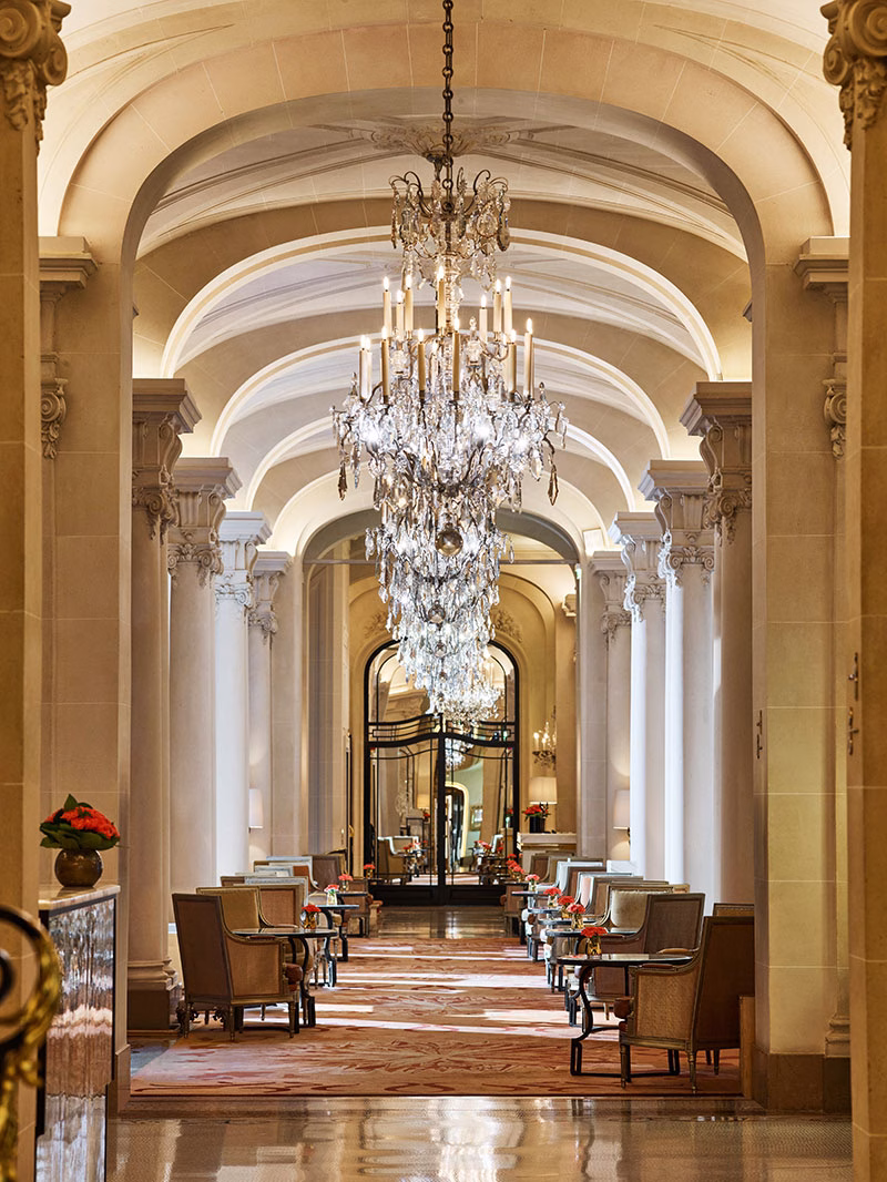 Blick durch den majestätischen, langgezogenen Flur des Restaurants La Galerie, geprägt von klassischen Rundbögen, einer Reihe opulenter Kristallkronleuchter, eleganten Sitzgruppen an den Seiten und edlen Marmorsäulen