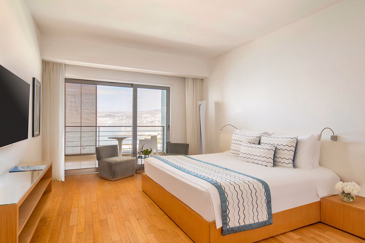 Schlafzimmer der Executive Suite im Großes helles Badezimmer in der Executive Panoramic Suite des Kempinski Hotel Aqaba Red Sea mit im Boden eingelassenen Whirlpool mit Bett, Fernseher und großen Fensterfronten, die den Blick auf das Meer eröffnen