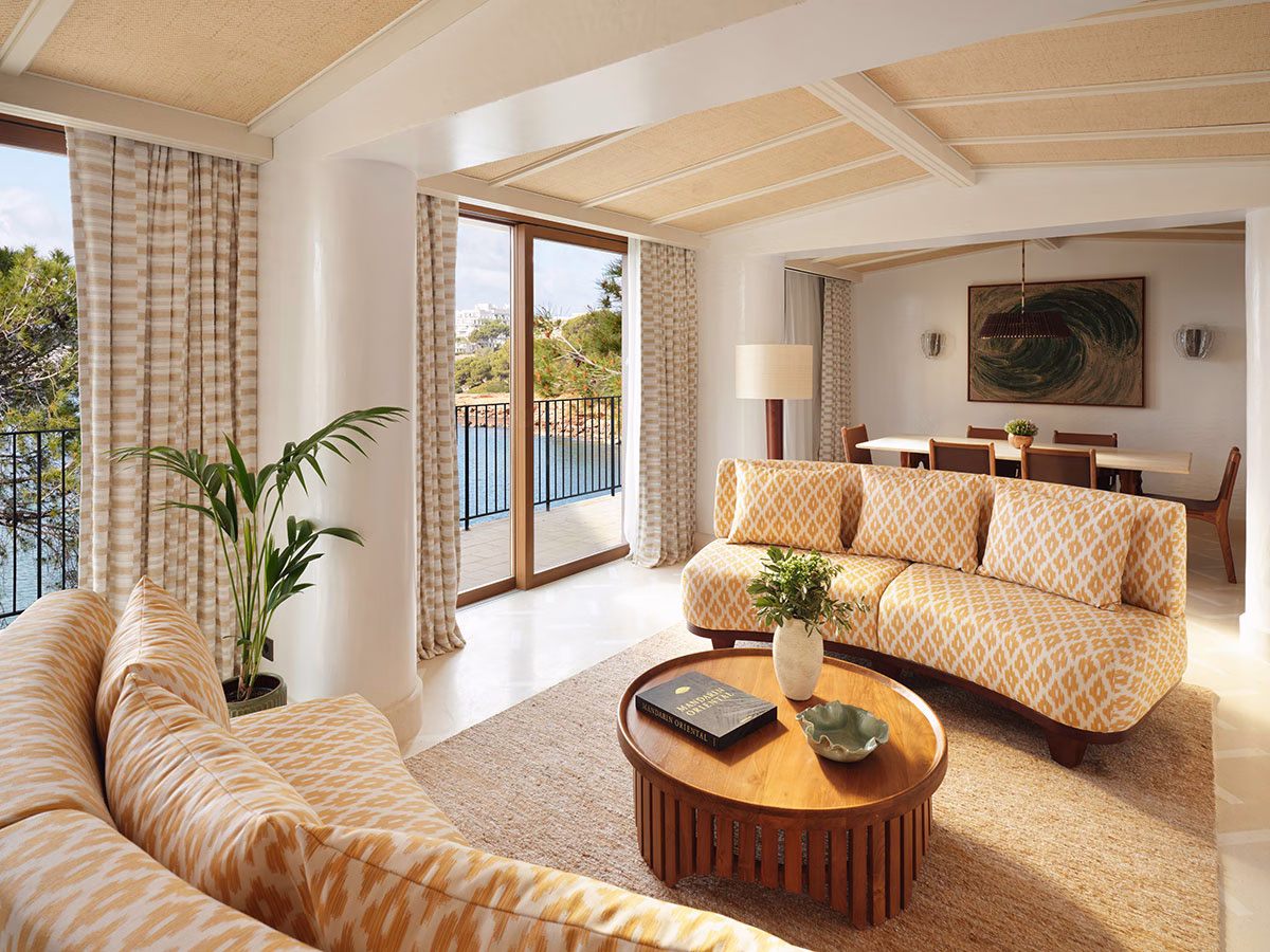 Lichtdurchfluteter Wohnbereich einer Suite im Mandarin Oriental Punta Negra mit gemusterten gelb-weißen Sofas, einem runden Holz-Couchtisch und großen Glasschiebetüren zum Balkon mit Meerblick