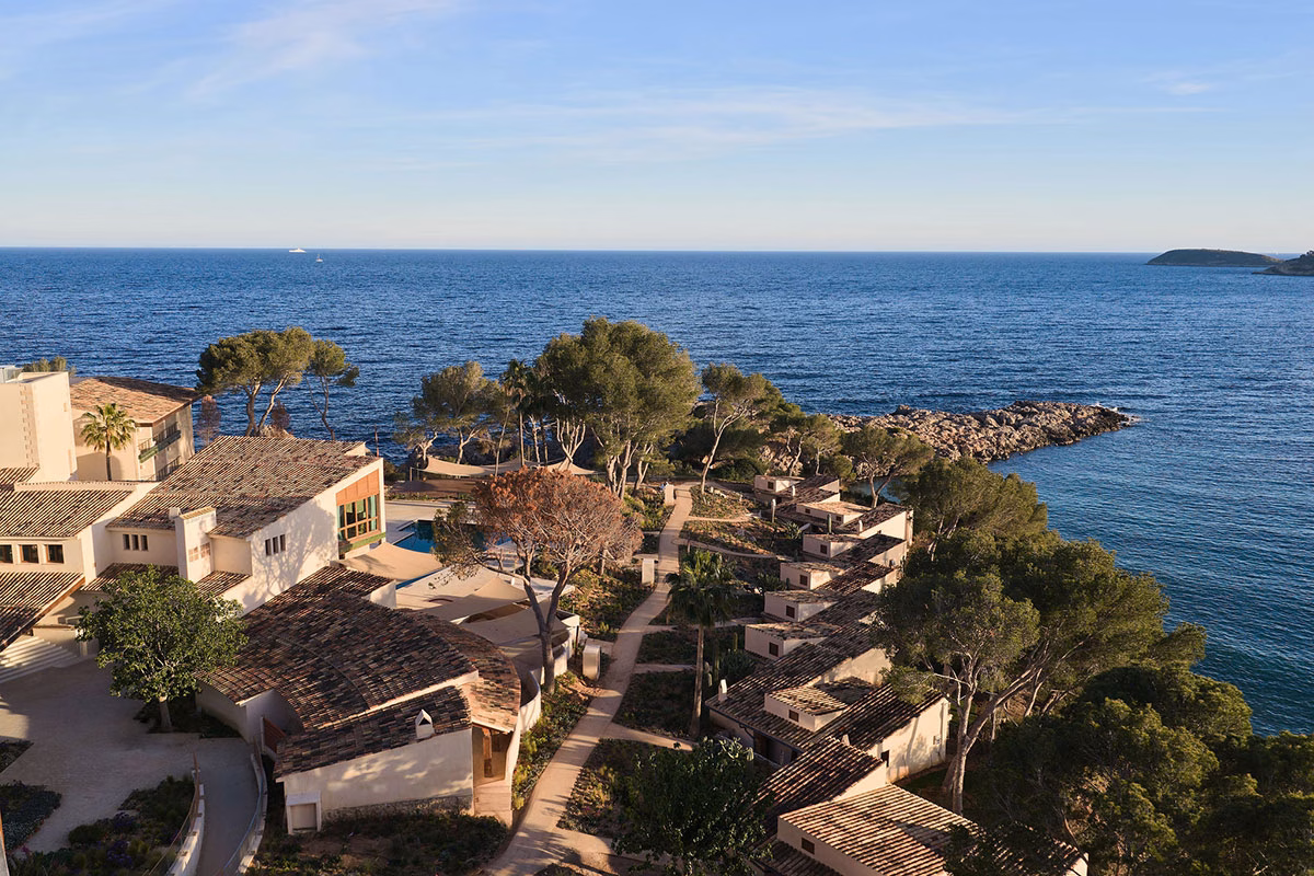 Erhöhte Außenansicht des Hotelkomplexes Mandarin Oriental Punta Negra, dessen flache Bungalows mit traditionellen mallorquinischen Ziegeldächern in eine üppige Pinienlandschaft direkt an der felsigen Meeresküste eingebettet sind