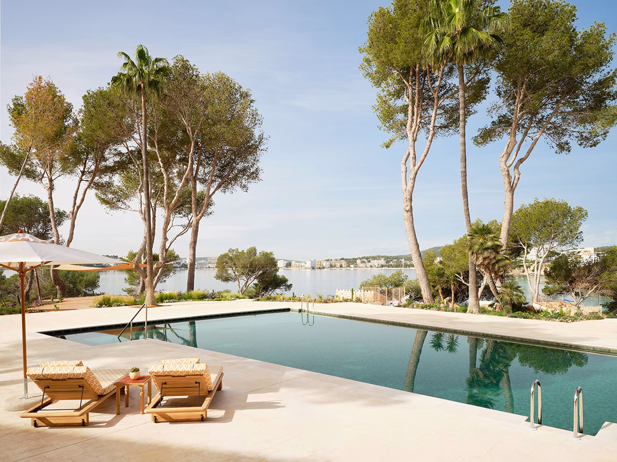Ein großer, rechteckiger Außenpool im Mandarin Oriental Punta Negra, gesäumt von hellen Fliesen, zwei eleganten Sonnenliegen unter einem Sonnenschirm und hohen, schlanken Palmen mit Blick auf das ruhige Meer im Hintergrund