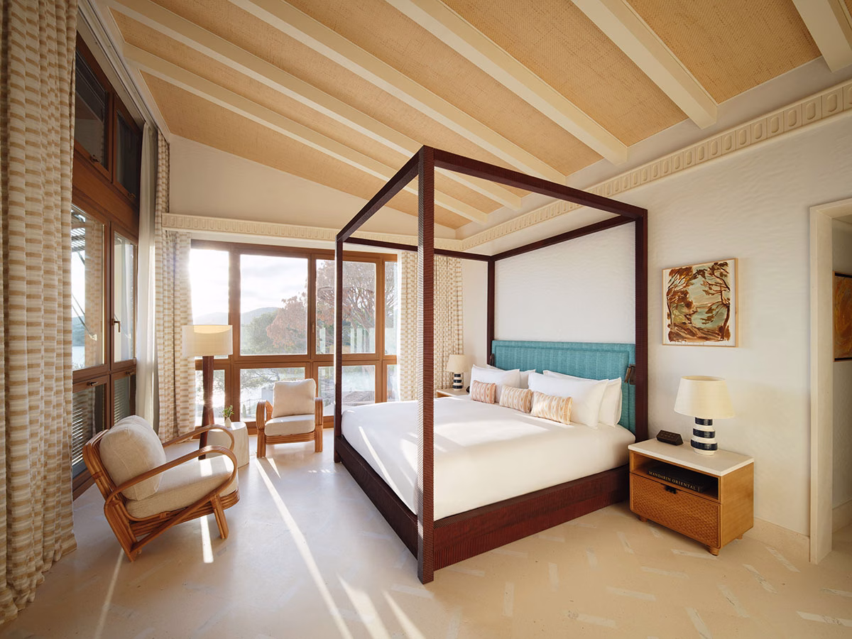 Das luxuriöse Schlafzimmer der Punta Negra Suite mit einem großen Himmelbett aus dunklem Holz, einer hellblauen Zimmerwand als Kopfteil, Rattan-Sesseln und einer bodentiefen Fensterfront