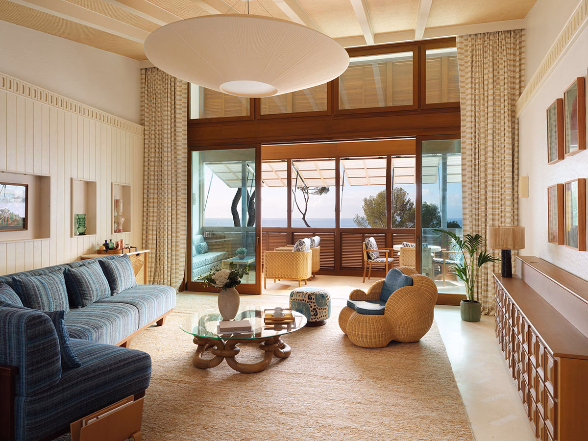 Großzügiger Wohnbereich der Punta Negra Suite im Mandarin Oriental Punta Negra mit einem blau-weiß gestreiften Sofa, einem gläsernen Couchtisch, Flechtsesseln und weit geöffneten Türen zur Terrasse mit Meerblick