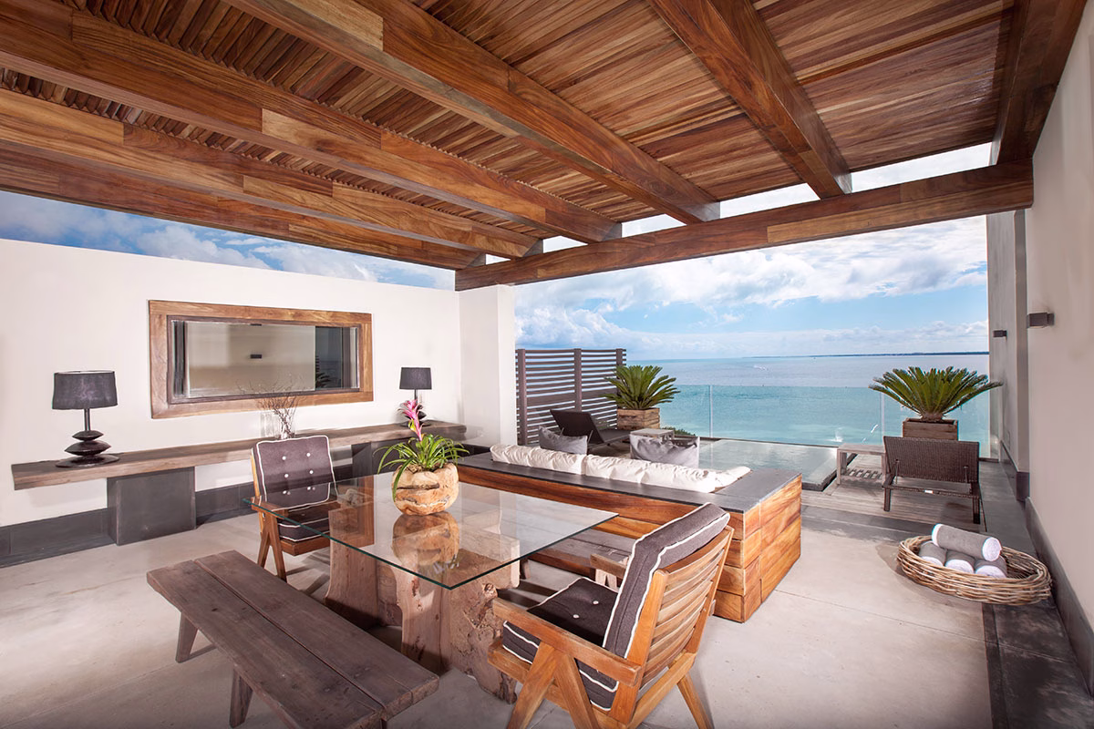 Großzügige, holzverkleidete Terrasse im NIZUC Resort & Spa mit einer gemütlichen Korb-Eckcouch, einem massiven Holz-Esstisch mit Glasplatte und freiem Blick auf das karibische Meer