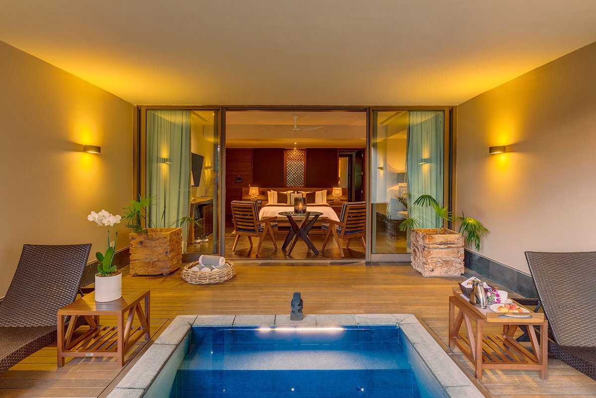Ein privater, in die Terrasse eingelassener Tauchbecken-Pool einer Garden Junior Suite im NIZUC Resort & Spa, flankiert von Loungeliegen und großen Holz-Pflanzkübeln mit Blick in den warm erleuchteten Schlafbereich