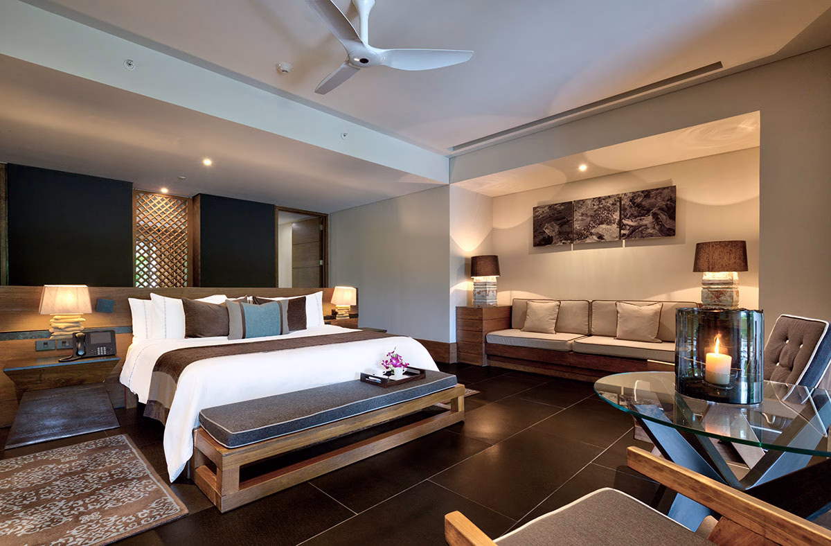 Geräumige und stilvoll ausgeleuchtete Suite im NIZUC Resort & Spa, ausgestattet mit einem großen Doppelbett, einer gemütlichen Polsterecke im Hintergrund, einem modernen Glastisch im Vordergrund und einem Deckenventilator