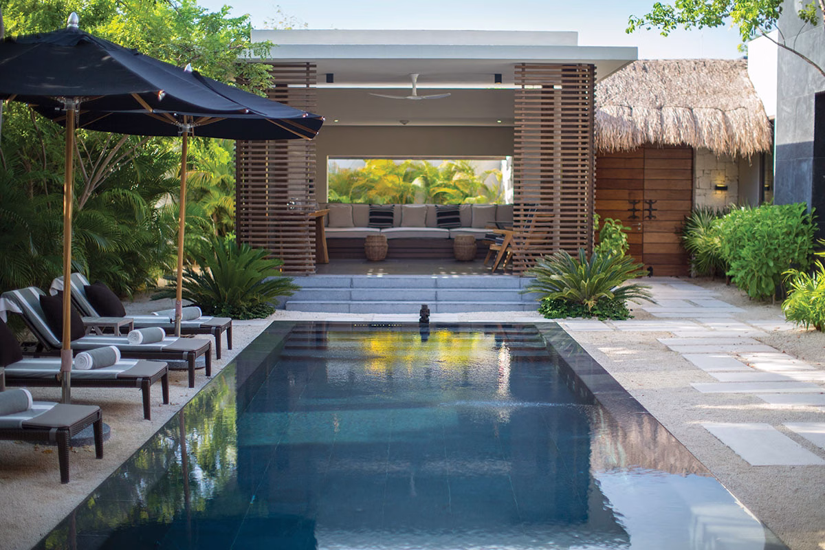 Ein privater, von Palmen umgebener Pool im NIZUC Resort & Spa mit gemütlichen Sonnenliegen im Sand und einem erhöht liegenden, modernen Lounge-Pavillon mit Holzlamellen im Hintergrund