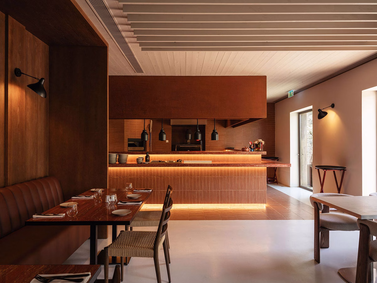 Moderne, warme Innenansicht des ÀTERRA Restaurants im Octant Douro mit dunkelbraunen Holzwänden, einer elegant beleuchteten Theke in Terrakotta-Optik und gemütlichen Sitzbereichen mit Lederbänken