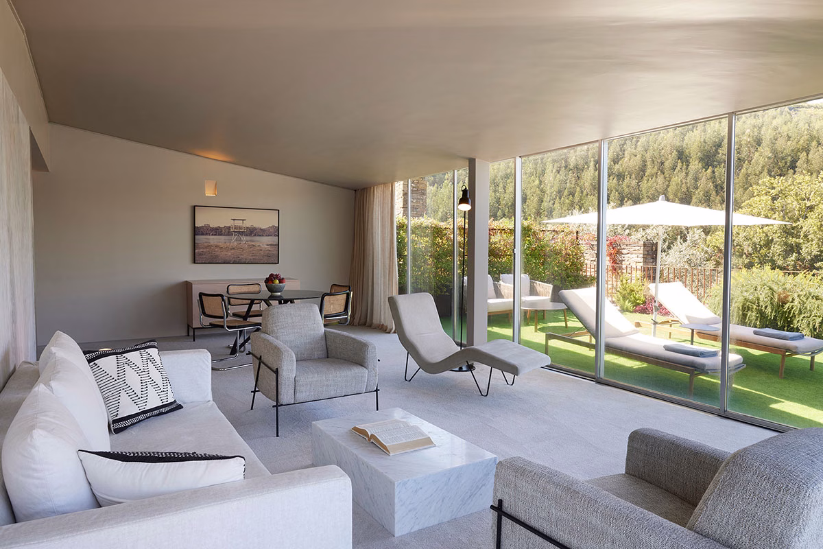 Das lichtdurchflutete, großzügige Wohnzimmer einer Panoramic Suite im Octant Douro mit weißen Sofas, stilvollen Sesseln und einer breiten Glasfront mit Blick auf eine begrünte Privatterrasse mit Sonnenliegen