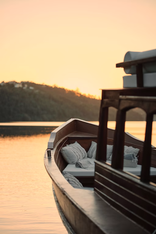 Nahaufnahme des hölzernen Bugs eines traditionellen Rabelo-Boots, ausgestattet mit gemütlichen Kissen und Decken, während der Fahrt auf dem Douro-Fluss im goldenen Licht des Sonnenuntergangs