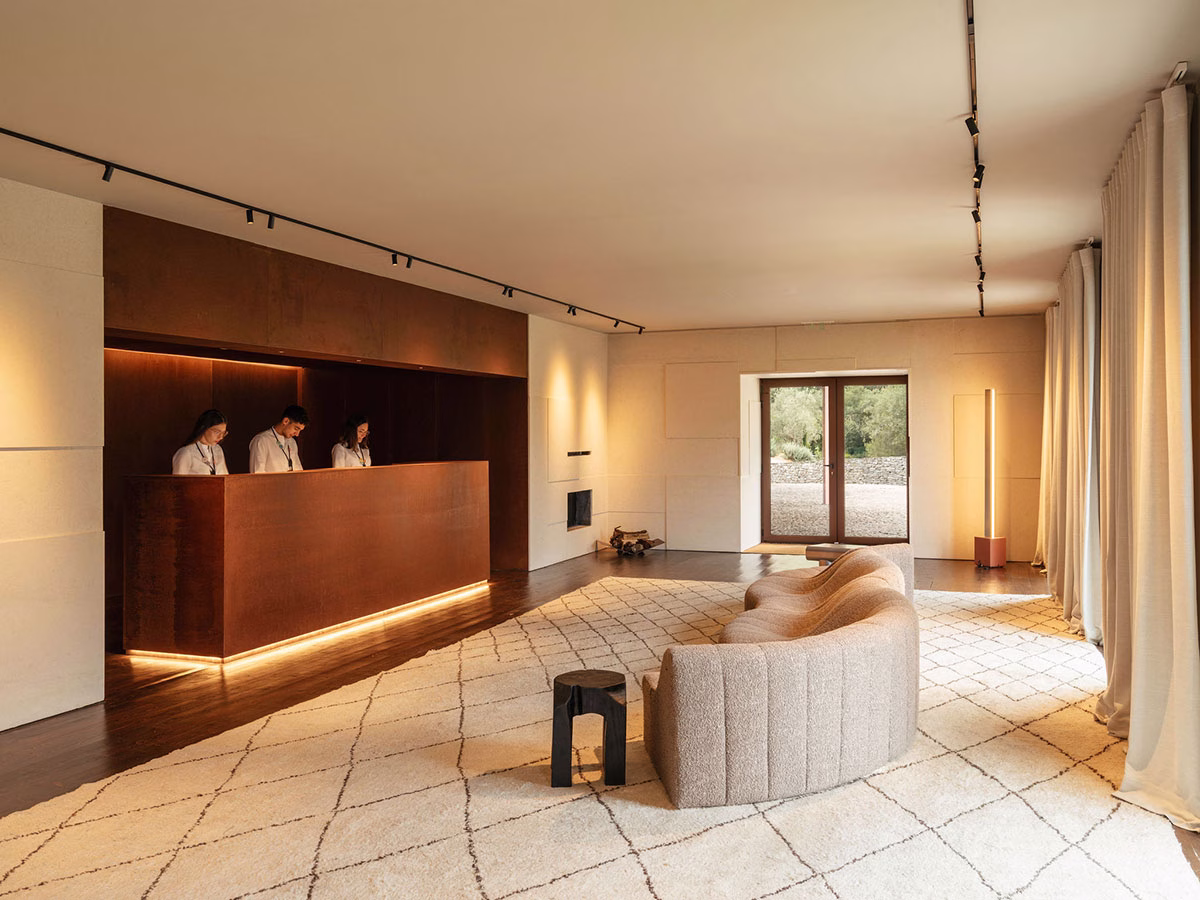 Der elegante Rezeptionsbereich im Octant Douro mit einem langen, minimalistischen Empfangstresen in Rostoptik, drei Hotelmitarbeitern und einem geschwungenen, hellen Design-Sofa auf einem gemusterten Teppich