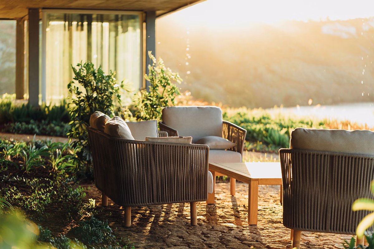 Eine gemütliche Outdoor-Lounge-Ecke im Octant Douro mit beigen Sesseln und einem Holztisch auf einer Naturstein-Terrasse, sanft beschienen von der tiefstehenden Abendsonne