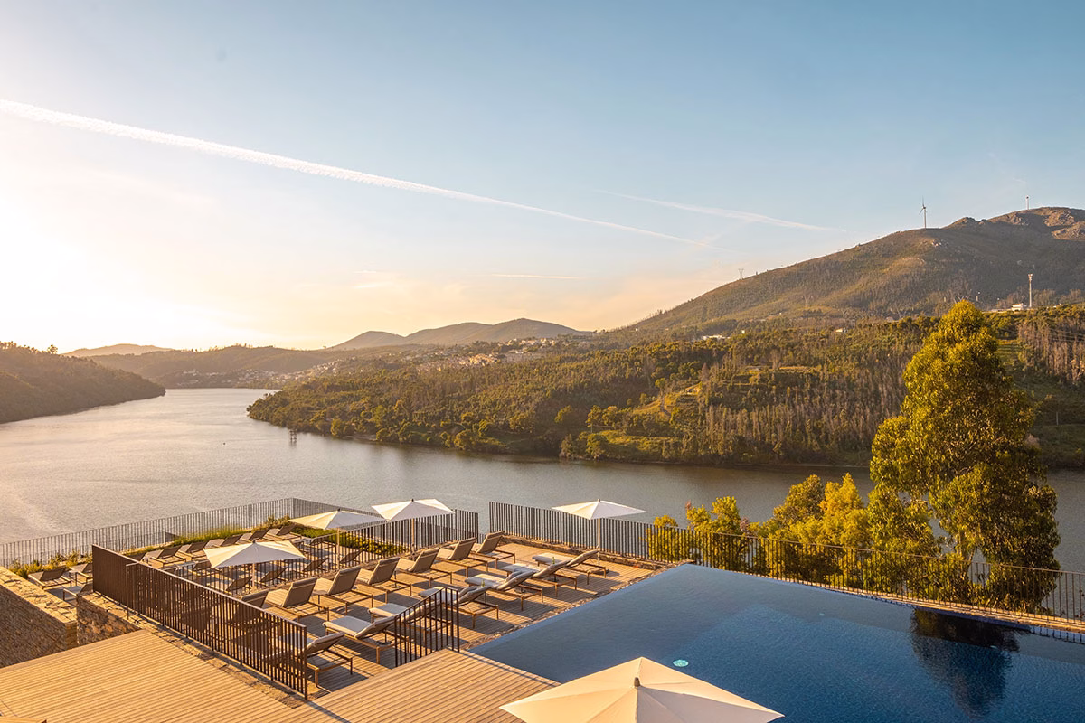 Ein großer Infinity-Außenpool auf der oberen Terrasse des Octant Douro mit zahlreichen Sonnenliegen unter weißen Schirmen, fotografiert im goldenen Licht des Sonnenuntergangs über dem Fluss