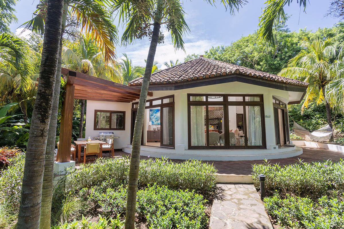 Außenansicht einer runden Garden View Casita im Rancho Santana mit traditionellem Ziegeldach, umgeben von tropischen Palmen, üppigem Grün und einer überdachten Holzterrasse mit Esstisch