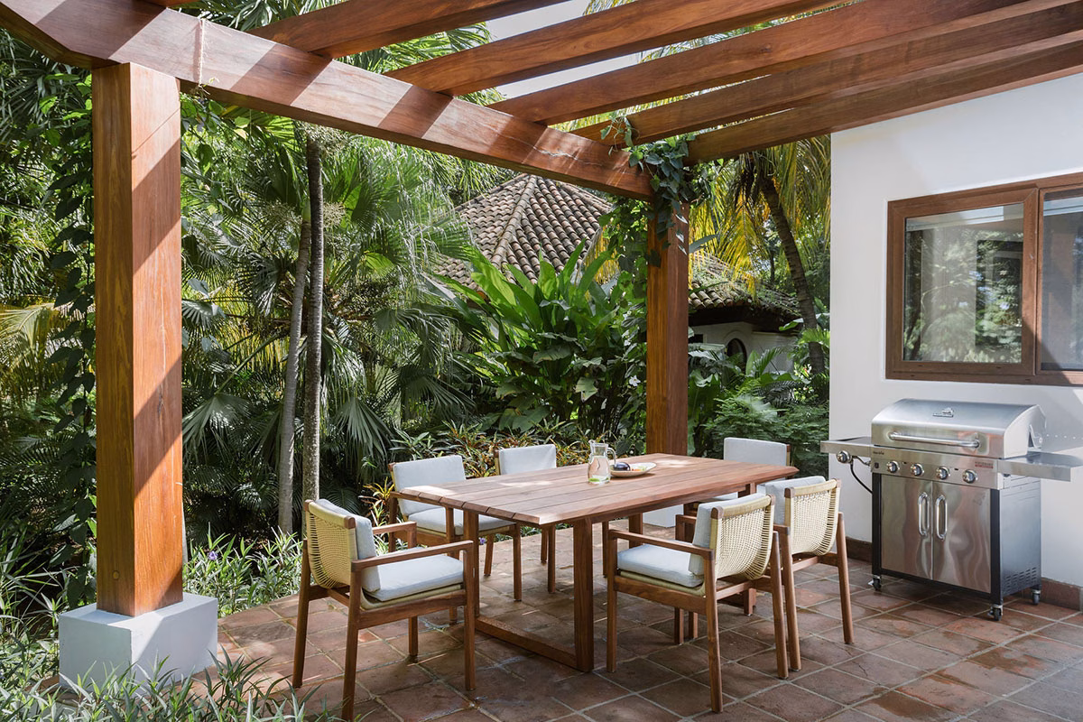 Schattige Holzpergola auf der Terrasse einer Garden View Casita im Rancho Santana, ausgestattet mit einem großen Esstisch aus Holz, bequemen Sesseln und einem Edelstahl-Gasgrill