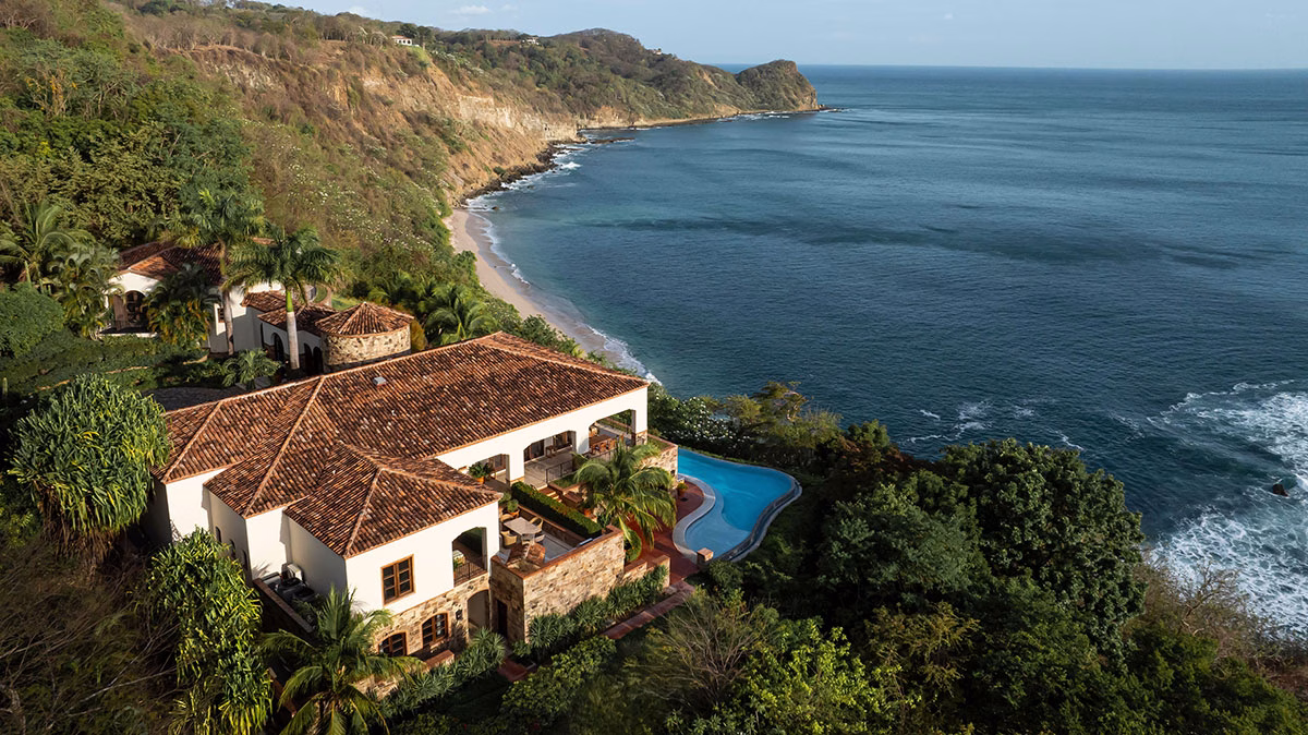 Spektakuläre Luftansicht der Villa Escondida aus der Luxury Collection, die mit einem geschwungenen Infinity-Pool auf einer Klippe hoch über dem blauen Ozean und dem Sandstrand thront