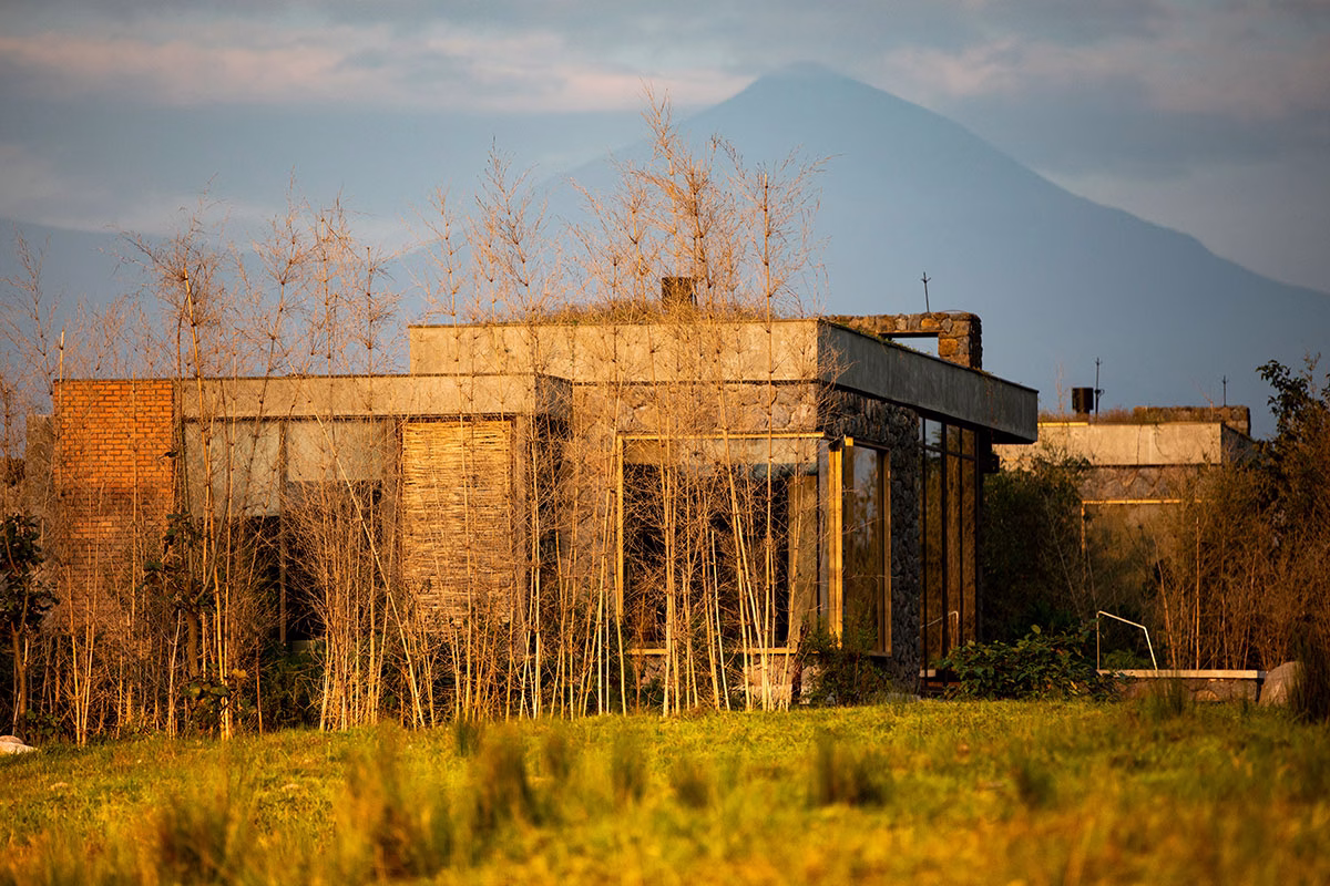 Außenansicht des Singita Kataza House aus Naturstein und Ziegeln, harmonisch eingebettet in eine Landschaft mit feinen Bambussträuchern vor der Kulisse eines majestätischen Vulkans