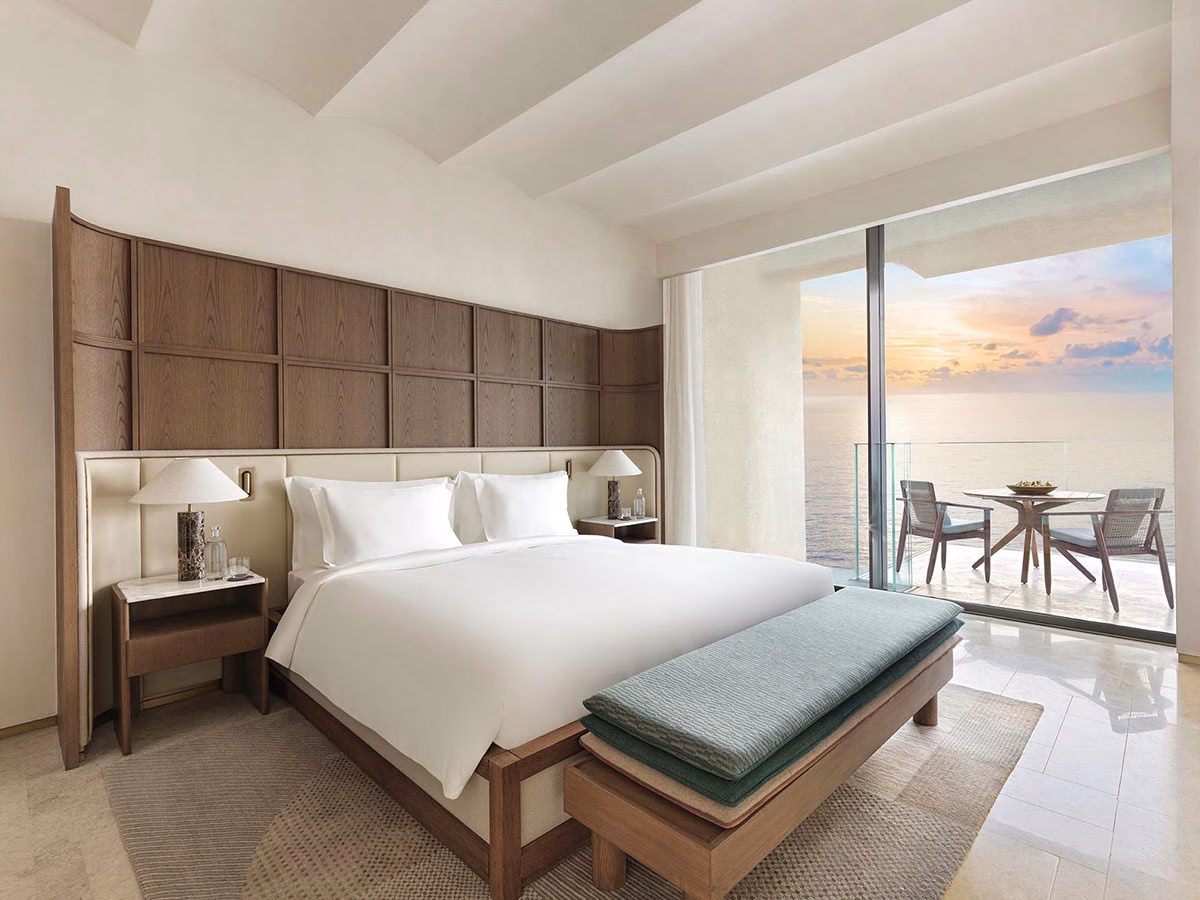 Exklusives Schlafzimmer der Breeze Suite mit komfortablem Doppelbett, bodentiefen Fenstern mit direktem Meerblick bei Sonnenuntergang und Zugang zu einem möblierten Balkon