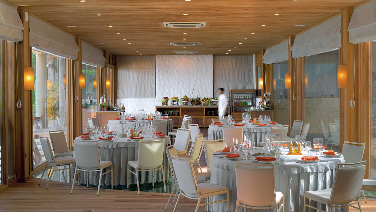 Veranstaltungsraum im Bankett-Stil mit runden Tischen, eingedeckt für ein formelles Essen, unter einer warm beleuchteten Holzdecke mit bodentiefen Glaswänden