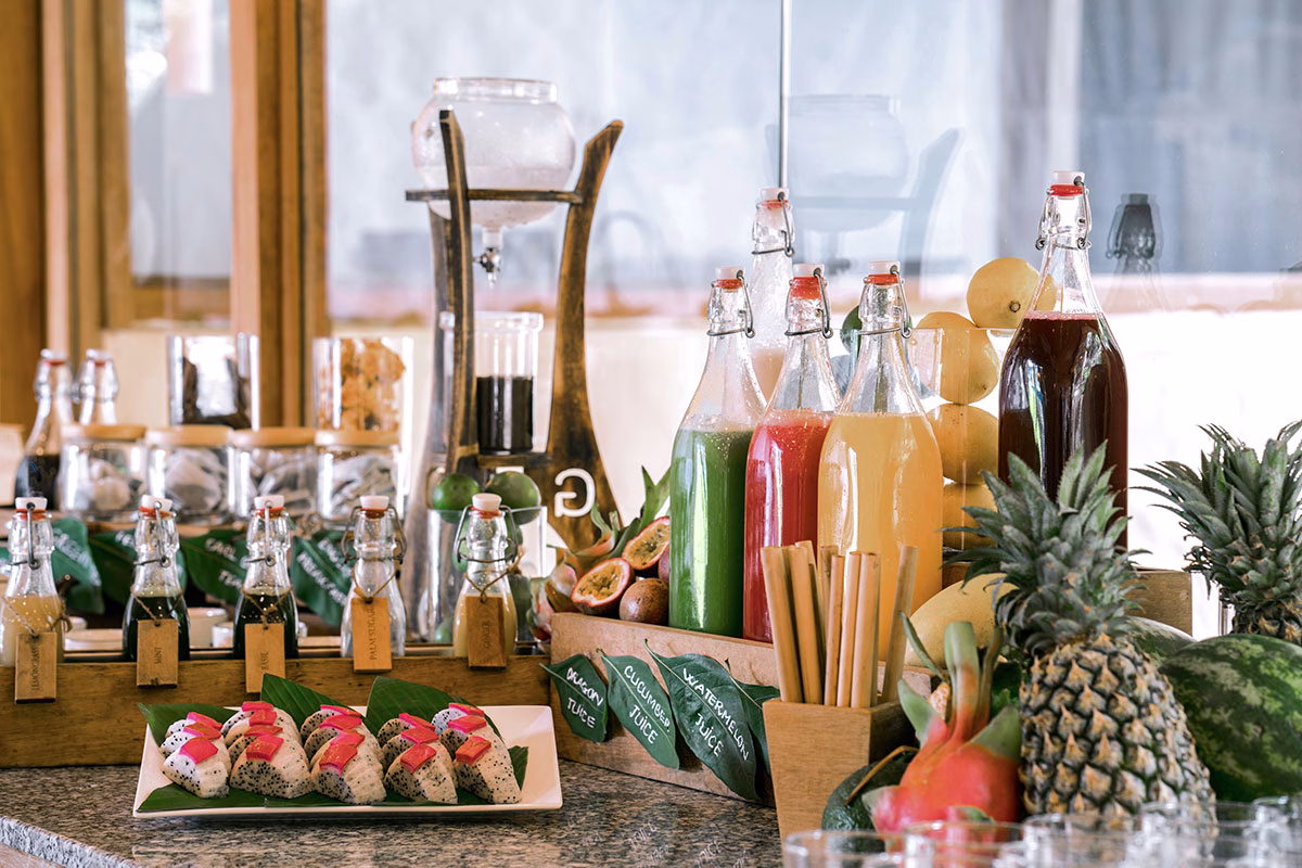 Ansprechendes Buffet für eine Kaffeepause mit einer Auswahl an frischen Säften in Glasflaschen, aufgeschnittener Drachenfrucht, Ananas und nachhaltigen Bambusstrohhalmen