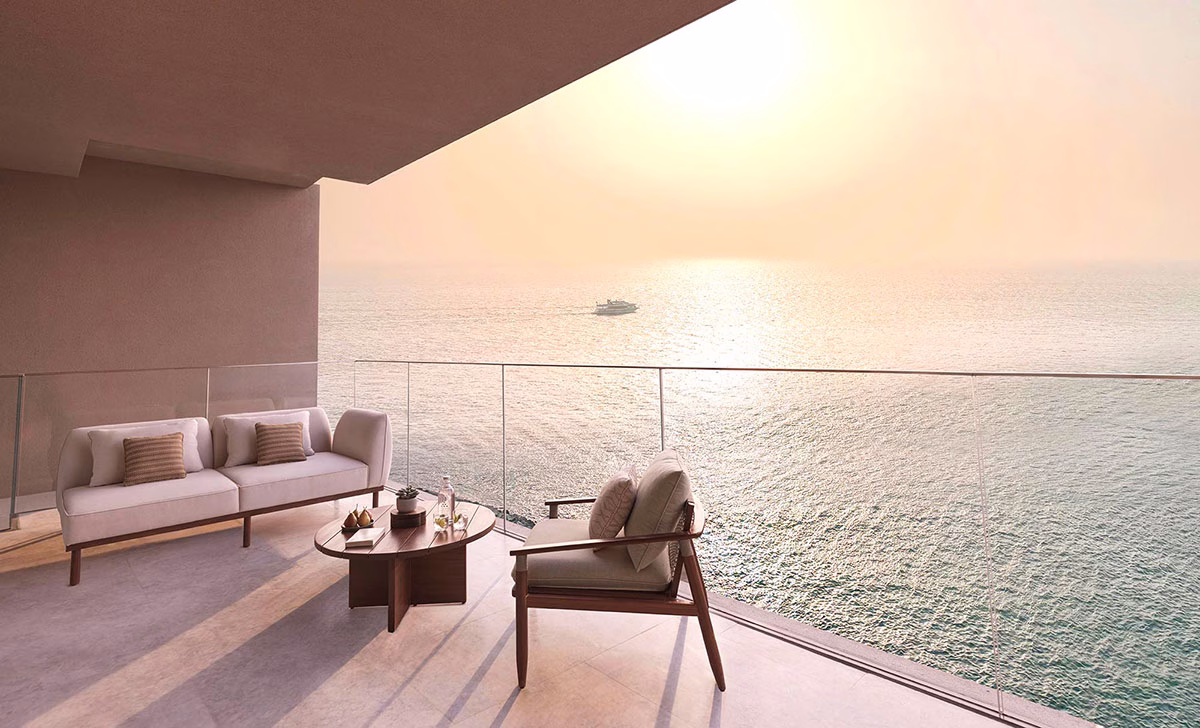 Möblierte Balkon-Terrasse des Three Bedroom Pool Retreats im Six Senses The Palm Dubai mit einem eleganten Outdoor-Sofa, einem Holzsessel und einem weiten Panorama-Blick über das glitzernde Meer bei goldenem Sonnenuntergang