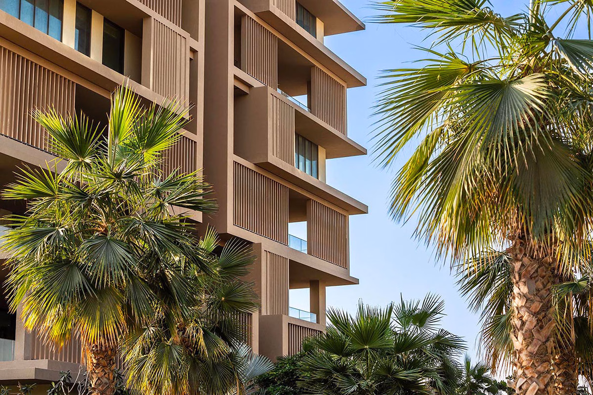 Architektonisches Detail des Six Senses The Palm mit Blick auf die strukturierten Balkone und vertikalen Holzelemente, umgeben von grünen Palmenblättern vor blauem Himmel