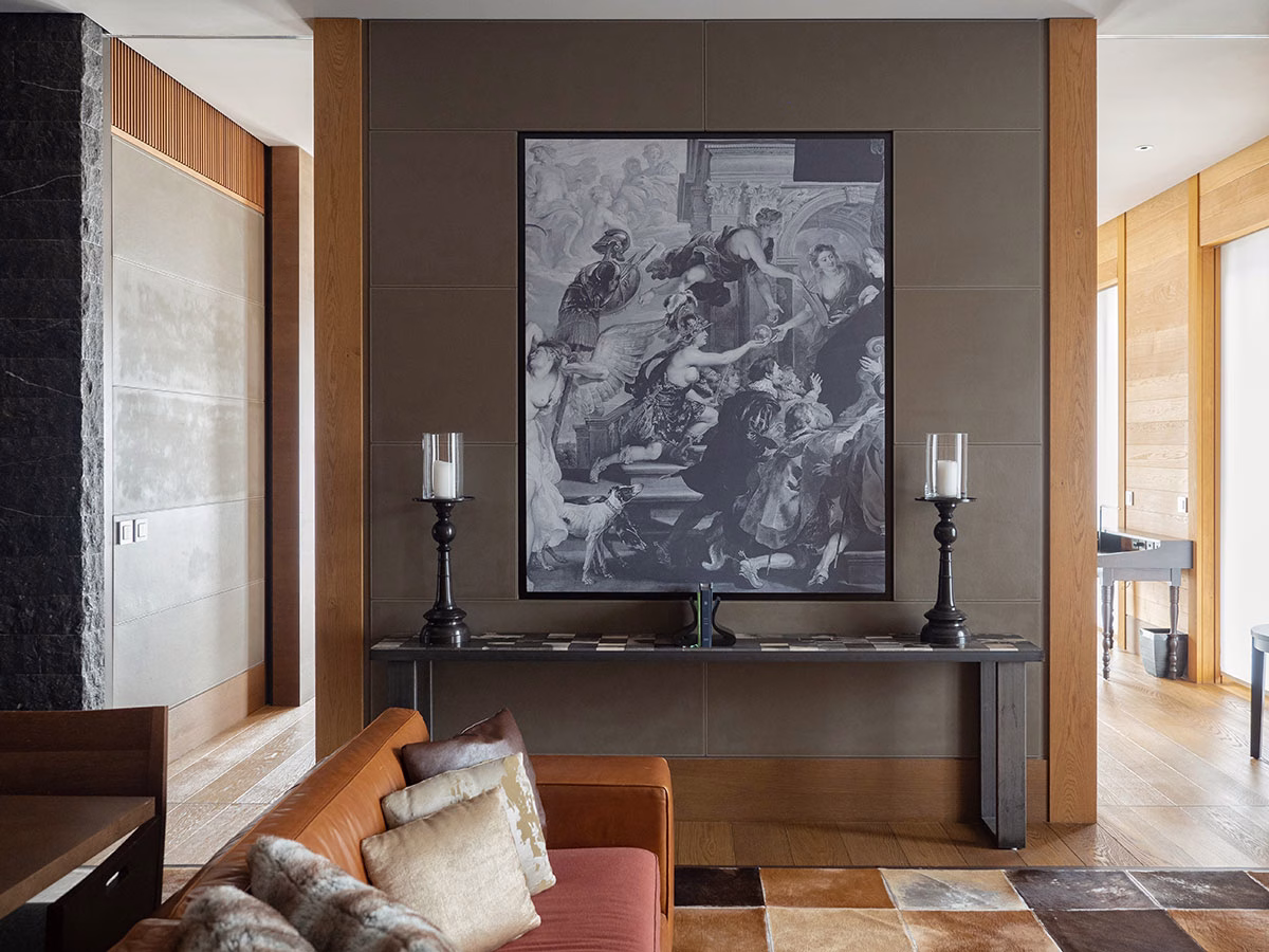 Elegantes Interieur der Gemsstock-Suite im The Chedi Andermatt mit einem cognacfarbenen Ledersofa, einem Kuhfell-Teppich und einem großen, historischen Schwarz-Weiß-Gemälde an der mit Leder bespannten Wand