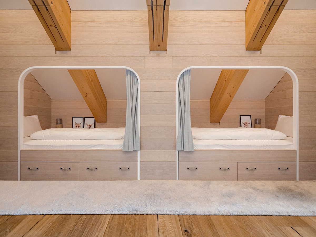 Modernes Kinderzimmer in der Gotthard-Suite des The Chedi Andermatt mit zwei eingebauten, gemütlichen Alkoven-Betten in einer hellen Holzwand unter massiven Dachbalken
