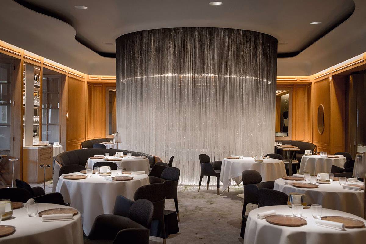Das moderne, minimalistisch angehauchte Restaurant Alain Ducasse at The Dorchester mit elegant eingedeckten, runden Tischen und einem spektakulären, raumhohen Vorhang aus schimmernden Lichterfäden im Zentrum