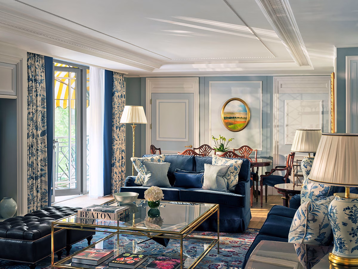 Ein stilvoller Hotelsalon im The Dorchester, eingerichtet mit tiefblauen Samtsofas, klassisch gemusterten Kissen, blau-weißen Porzellanlampen und einem Couchtisch aus Glas und Gold