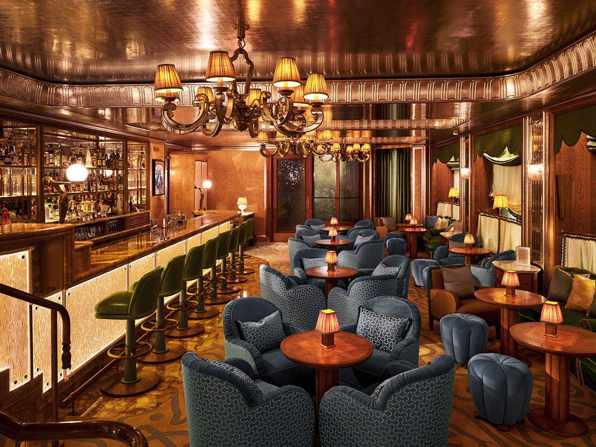 Die stimmungsvolle Vesper Bar im The Dorchester mit einer glänzenden Decke in Blattschgold, gemütlichen blauen Mustertesseln, grünen Barhockern an der Theke und einem großen, klassischen Kronleuchter