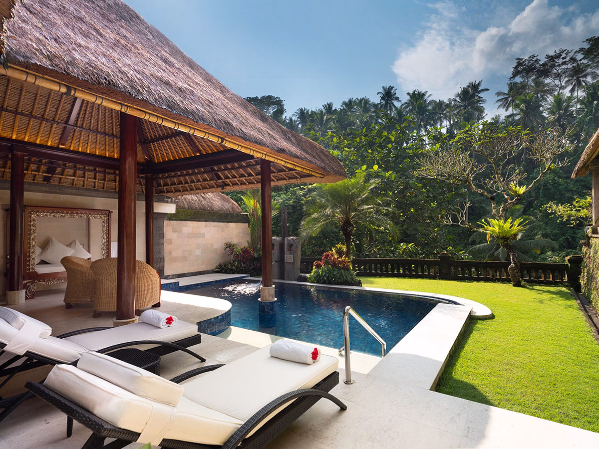 Der private Außenbereich der Elephant Villa im Viceroy Bali mit zwei Sonnenliegen, einem tiefblauen Infinity-Pool und einer gemütlichen Sitzecke unter einem balinesischen Reetdach, umgeben von einem grünen Garten