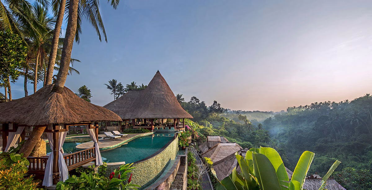 Der große Infinity-Hauptpool des Viceroy Bali mit einer geschwungenen Poolbar unter einem markanten Reetdach, eingebettet in die tropische Dschungellandschaft von Ubud am frühen Morgen
